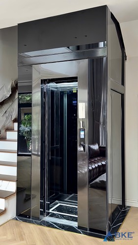 Thang máy lồng kính khung đen đặt cạnh cầu thang bộ, lấy sáng từ khoảng thông tầng